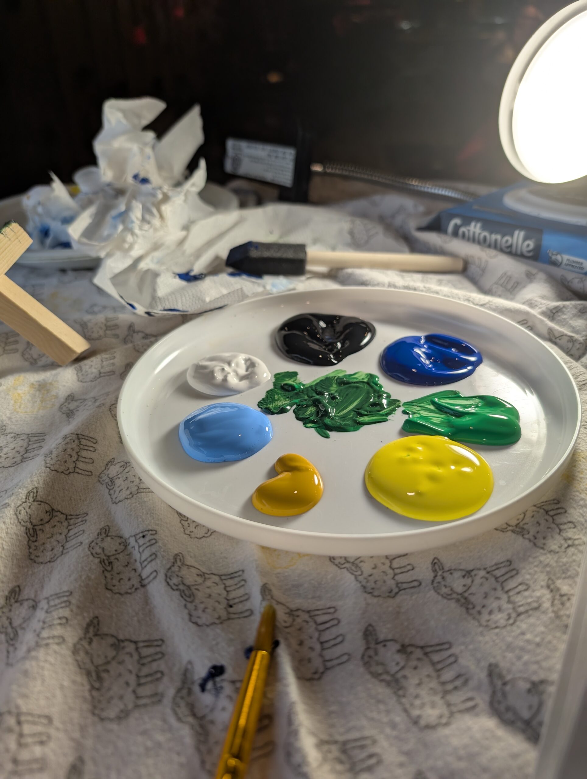 Globs of paint on a white tray next to paintbrushes and an easel